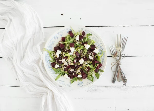 Beetroot salad with arugula, feta cheese, red salt and pumpkin seeds in vintage plate over white rustic wooden background, top view — Zdjęcie stockowe