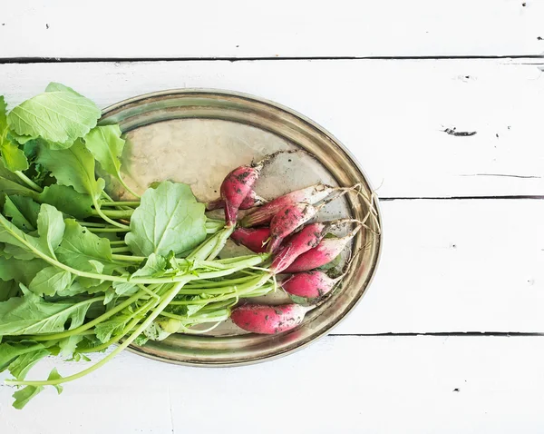 Bunch of fresh dirty garden radishes on vintage metal tray over rustic white wooden backdrop, top view — Stock Fotó