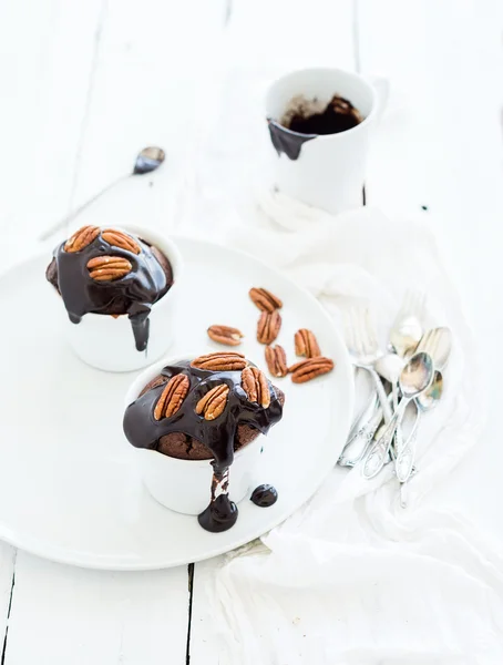 Sabrosas magdalenas marrones caseras con glaseado de ganache de chocolate y nueces de pacana en tazas de panadería separadas . —  Fotos de Stock