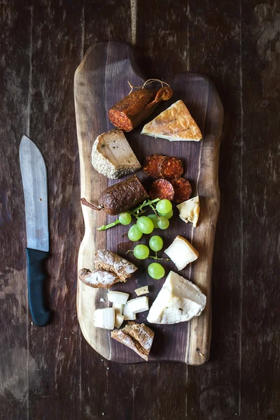 Wine appetizers set: meat and cheese selection, grapes, bread on rustic wooden board over dark wood background. Top view — Stock Photo, Image