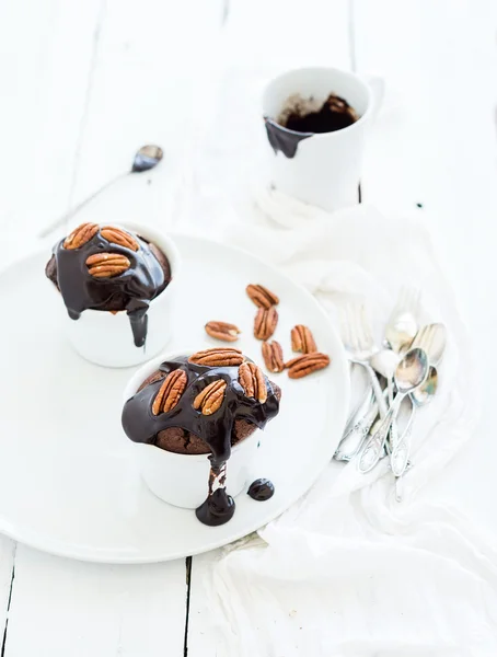Muffins bruns maison savoureux avec glaçage à la ganache au chocolat et noix de pécan dans des tasses de bakind séparées . Photos De Stock Libres De Droits