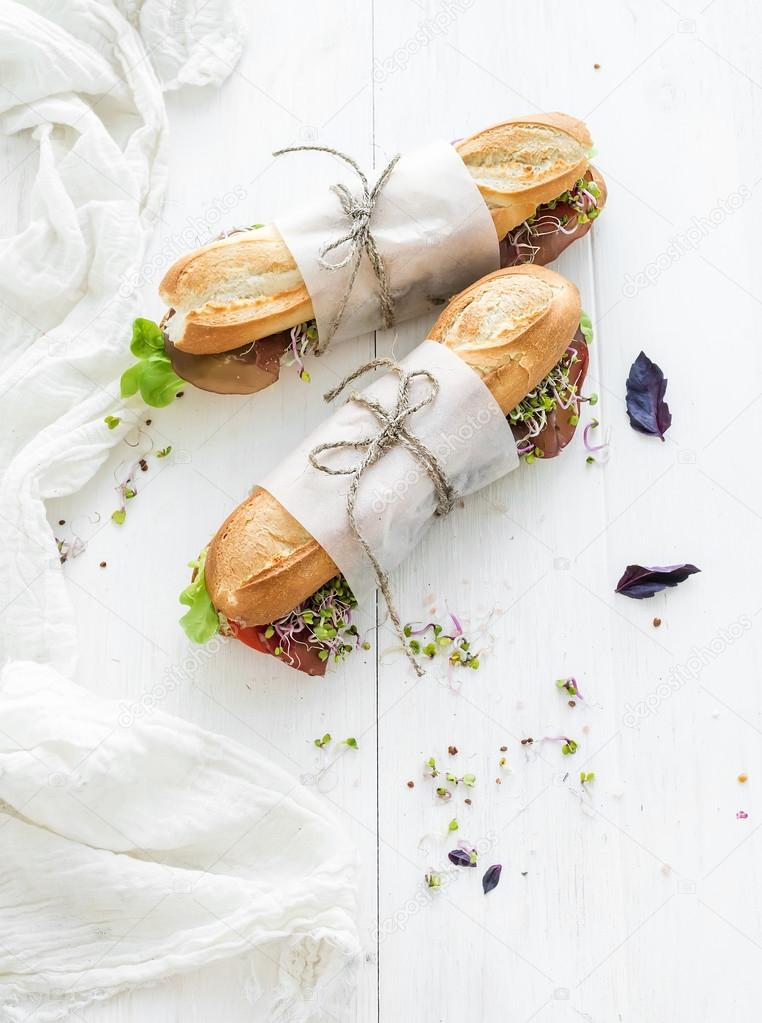 Sandwiches with beef, fresh vegetables and herbs over white wood backdrop, copy space