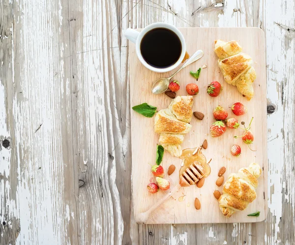 Čerstvě upečený mandlové croissanty s zahradní jahody a med na servírovací deska nad bílým rustikální dřevěné pozadí, pohled shora — Stock fotografie