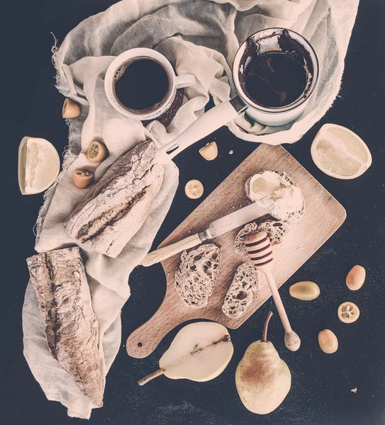 Conjunto de café da manhã: panela ou cezve de café, xícara, toalha de cozinha, fatias de baguete com creme de manteiga, amêndoas e mel em tábua de madeira rústica sobre fundo preto. Tons pastel — Fotografia de Stock