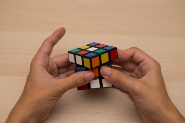 Elleri renkli bir yapboz. Rubik küpü 3 'er 3' er tahta bir masada yatıyor.