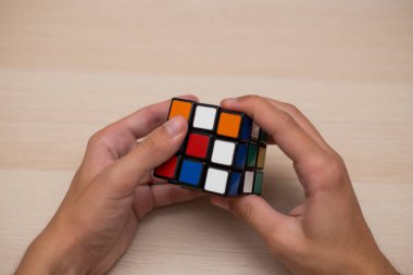 Elleri renkli bir yapboz. Rubik küpü 3 'er 3' er tahta bir masada yatıyor.