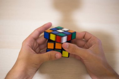 Elleri renkli bir yapboz. Rubik küpü 3 'er 3' er tahta bir masada yatıyor.