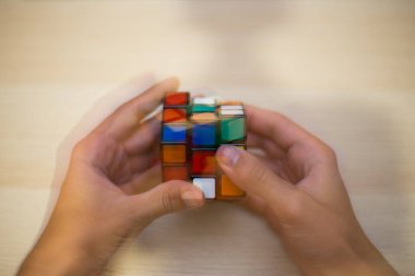 Elleri renkli bir yapboz. Rubik küpü 3 'er 3' er tahta bir masada yatıyor.