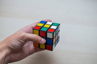 Elleri renkli bir yapboz. Rubik küpü 3 'er 3' er tahta bir masada yatıyor.