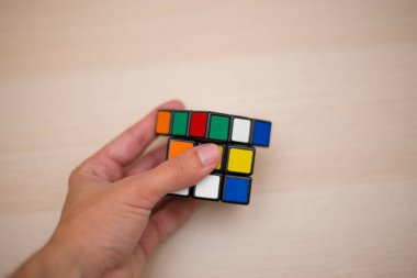 Elleri renkli bir yapboz. Rubik küpü 3 'er 3' er tahta bir masada yatıyor.