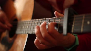 Kırmızı kazaklı bir adam kapalı mekanda akustik gitar çalar. Geniş açık bir deliğin yakın plan görüntüsü.