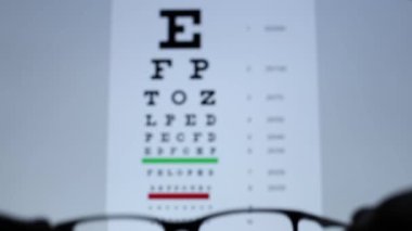 Bir insan gözlerine görüş gözlüğü getirir. Odak noktasından odak noktasına geçiliyor. Görüş test tablosunda ilk kişi görünümünü göster.