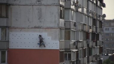 Şehirdeki çok katlı bir binanın ön cephesinin izolasyonu. Bir adam emniyet halatına tutunur ve binanın duvarını yalıtmak için çalışır..