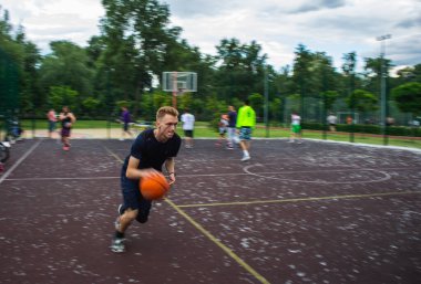 Genç kızıl saçlı bir adam yüksek hızda koşuyor ve top sürüyor. Gün içinde sokaktaki bir spor sahasında hareket bulanıklaştı.