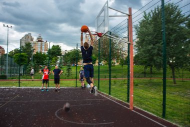 Genç kızıl saçlı bir adam yüksek hızda koşuyor ve top sürüyor. Gün içinde sokaktaki bir spor sahasında hareket bulanıklaştı.