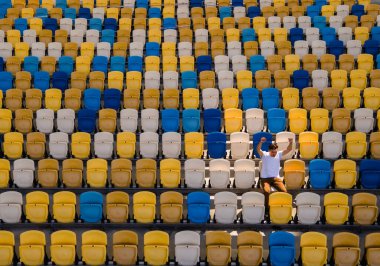 Beyaz tişörtlü genç bir adam boş bir futbol stadyumu tribününde şarkı söylüyor.