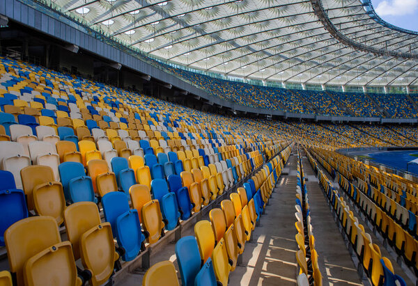 Empty rows of seats in a football olympic stadium with yellow and blue benches