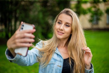 Kot ceketli güzel, modern moda bir kız telefonda selfie çekiyor.