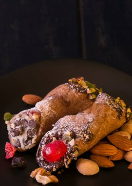 Siyah bir tabakta iki cannoli krem peynir ve şam fıstığından yapılmış geleneksel bir İtalyan tatlısı..