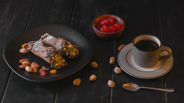 Siyah tabakta iki cannoli, krem peynirden yapılmış geleneksel İtalyan tatlısı ve fıstık ezmeli kahve..