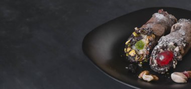 Siyah bir tabakta iki cannoli krem peynir ve şam fıstığından yapılmış geleneksel bir İtalyan tatlısı..