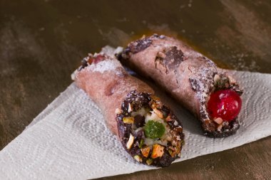 İki cannoli, krem peynirden yapılmış bir İtalyan tatlısı şam fıstığı ve çikolatalı. Sarı bir masada..