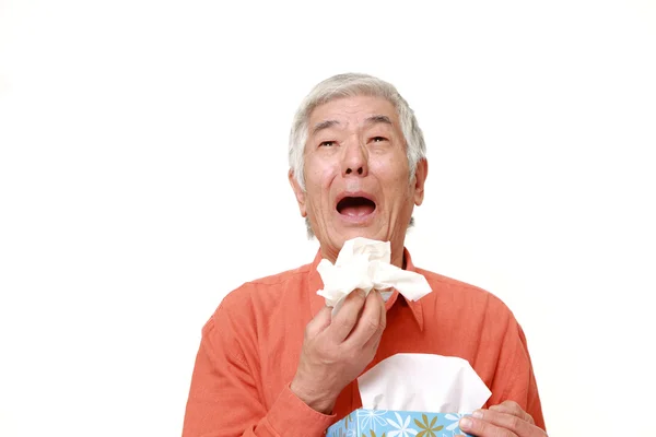 Старший японский мужчина с аллергией чихает в ткань — стоковое фото