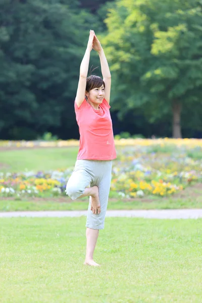 Japonesa mujer fuera haciendo yoga árbol pose — Foto de Stock