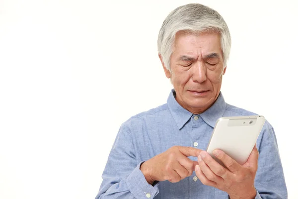 Старший японский человек, использующий планшетный компьютер выглядит запутанным — стоковое фото