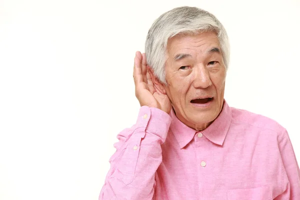Старший японский мужчина с рукой за ухом внимательно слушает — стоковое фото