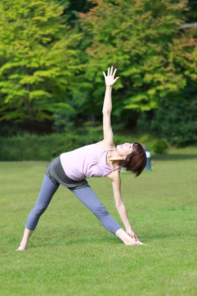 Japonesa mujer fuera haciendo yoga triángulo pose — Foto de Stock