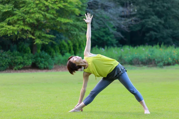 Japonesa mujer fuera haciendo yoga triángulo pose —  Fotos de Stock