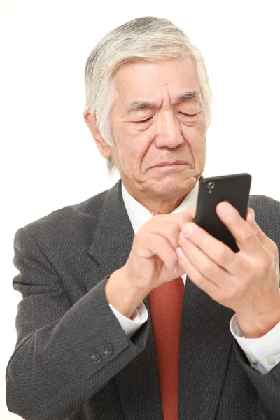 Senior japonés hombre de negocios usando teléfono inteligente buscando confundido —  Fotos de Stock