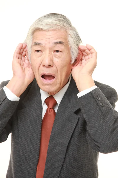 Empresário japonês sênior com a mão atrás da orelha ouvindo atentamente — Fotografia de Stock