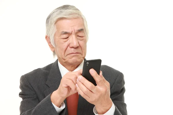 Senior japonés hombre de negocios usando teléfono inteligente buscando confundido —  Fotos de Stock