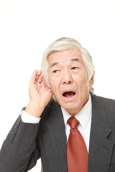 Empresário japonês sênior com a mão atrás da orelha ouvindo atentamente — Fotografia de Stock