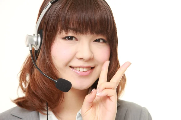 Joven mujer de negocios japonesa de call center con conjuntos de cabezas que muestran una señal de victoria —  Fotos de Stock