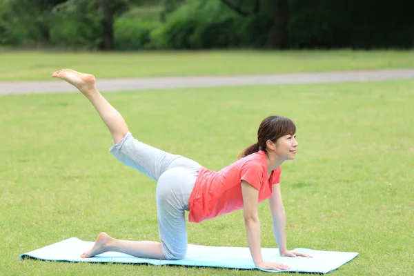 Japanese woman outside doing yoga cat pose — Stock Photo, Image