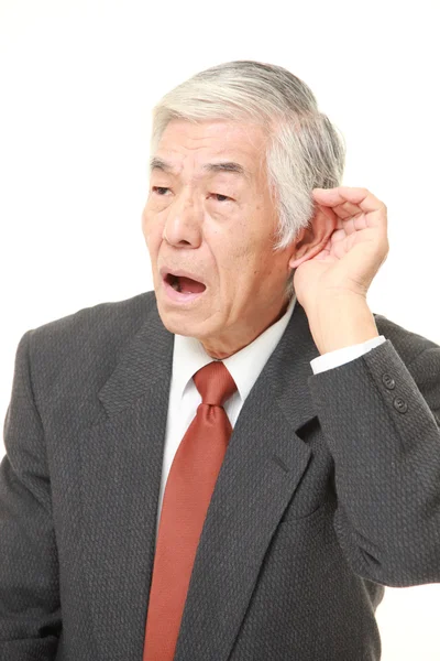 Ανώτερος ιαπωνικός επιχειρηματίας με το χέρι πίσω από το αυτί ακούει προσεκτικά — Φωτογραφία Αρχείου
