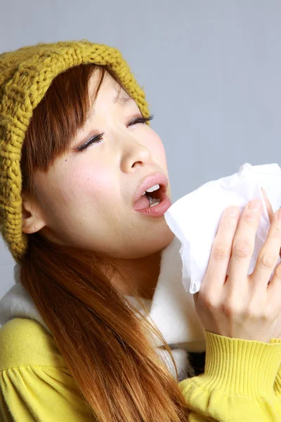 Young Japanese woman sneezing into tissue — Stock Photo, Image