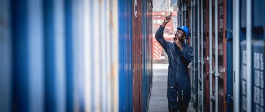 Mavi tulumlu, ithalat ve ihracat için nakliye konteynırlarını denetleyen siyah personel çalışanı..