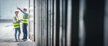 Sarı yelekli ve kasklı personel işçileri ithalat ve ihracat için içi boş nakliye konteynırlarını inceliyor..