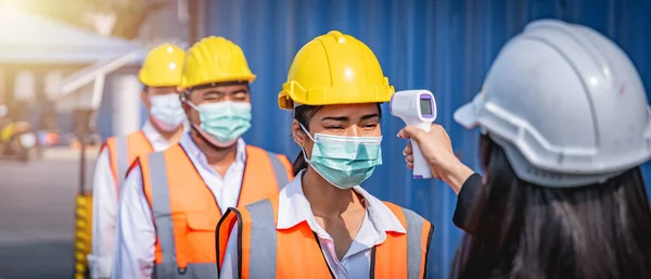 フェイスマスクを着用したエンジニアが職場に入る前に温度チェックのために並んでいます コロナウイルスのパンデミック 社会的距離 ロイヤリティフリーのストック画像