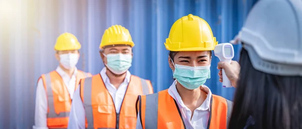 フェイスマスクを着用したエンジニアが職場に入る前に温度チェックのために並んでいます コロナウイルスのパンデミック 社会的距離 ストックフォト