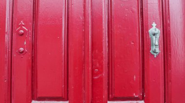 Pervazları olan kırmızı ahşap bir kapı, eski bir tokmağı var.