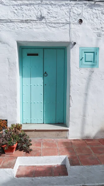 Entrance of a house in an Andalusian village, the door is made of wood with moldings and is painted turquoise, the facade is white, there are plants at the entrance and the floor is made of clay — Stock Image Entrance House Andalusian Village Door Made Wood Moldings Painted Turquoise Stock Photo