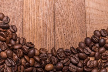 Ahşap bir yüzeye dağılmış, kahverenginin farklı tonlarında kavrulmuş kahve çekirdekleri. Tepede yazı için yer var. Kahve arkaplanı veya doku konsepti.