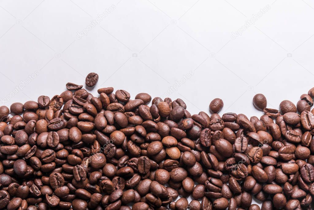 roasted coffee beans of various shades of brown scattered on a white surface with room for text on top. Coffee background or texture concept.