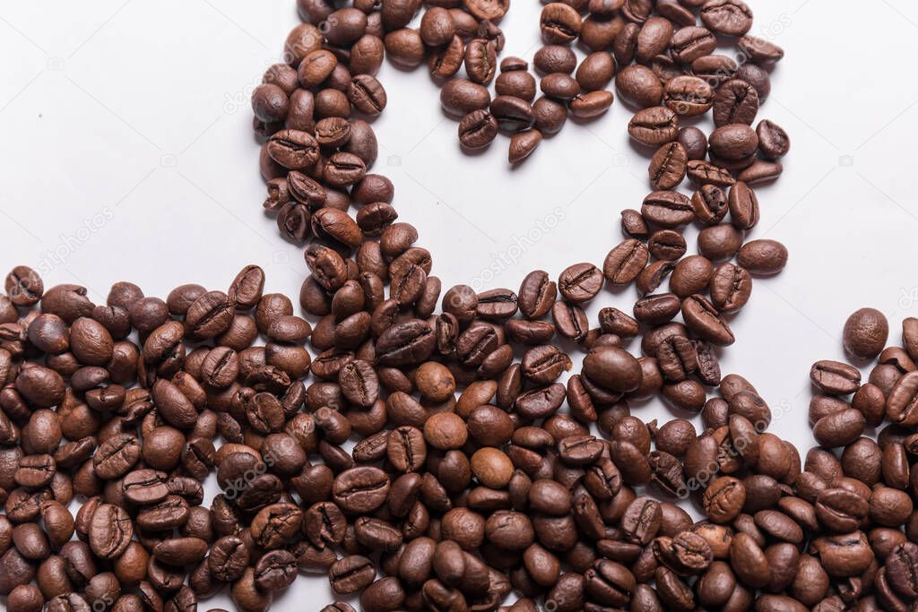 roasted coffee beans of different shades of brown scattered on a white surface forming a heart. Coffee background or texture concept and love of coffee.
