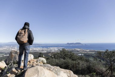 Bir dağın tepesinde kışın giyinmiş bir adam Algeciras Körfezi 'nin ve Cebelitarık Kayası' nın açık bir kış gününde manzarasını düşünür.